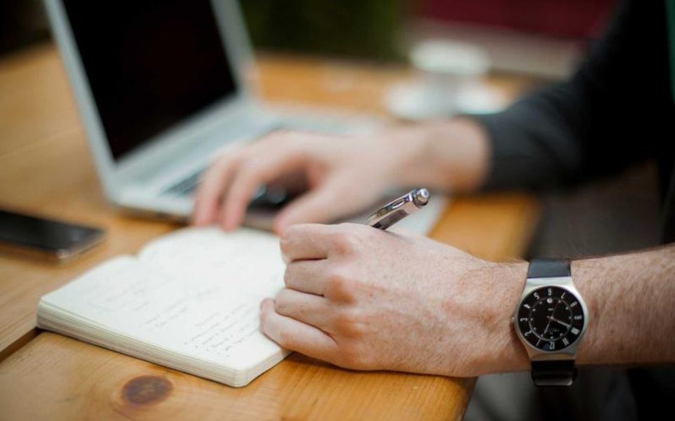 A person writing notes next to a wristwatch